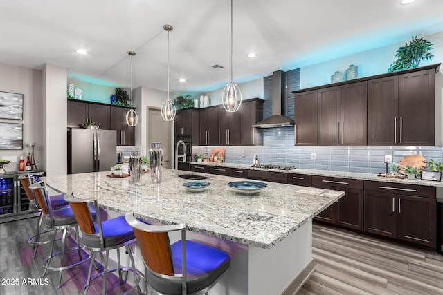 kitchen featuring tasteful backsplash, stainless steel appliances, a sink, dark brown cabinets, and wall chimney exhaust hood