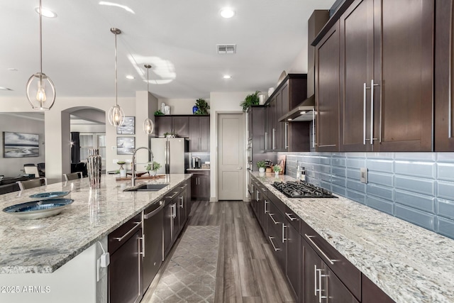 kitchen with range hood, decorative backsplash, a sink, dark brown cabinets, and appliances with stainless steel finishes