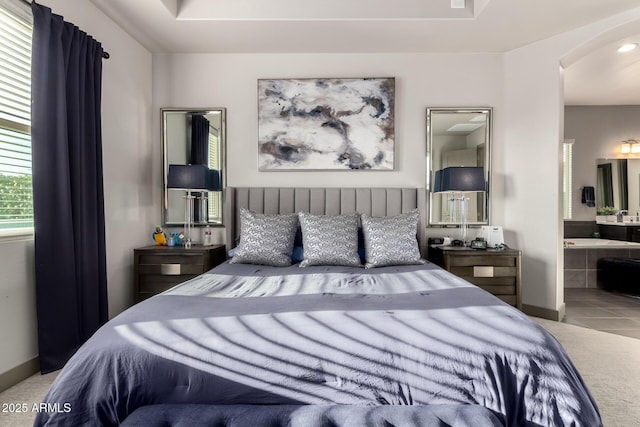 carpeted bedroom with tile patterned floors, arched walkways, connected bathroom, and baseboards