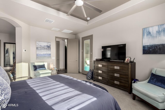 carpeted bedroom with a ceiling fan, arched walkways, a tray ceiling, and visible vents