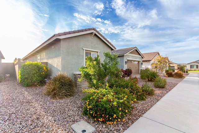 view of side of property with stucco siding, an attached garage, a tile roof, and a residential view