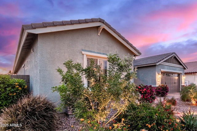 view of front of house with stucco siding, an attached garage, a tiled roof, and an outbuilding