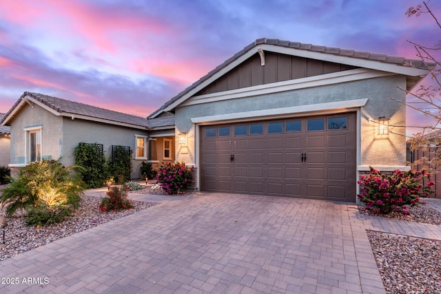 single story home with board and batten siding, stucco siding, decorative driveway, and a garage
