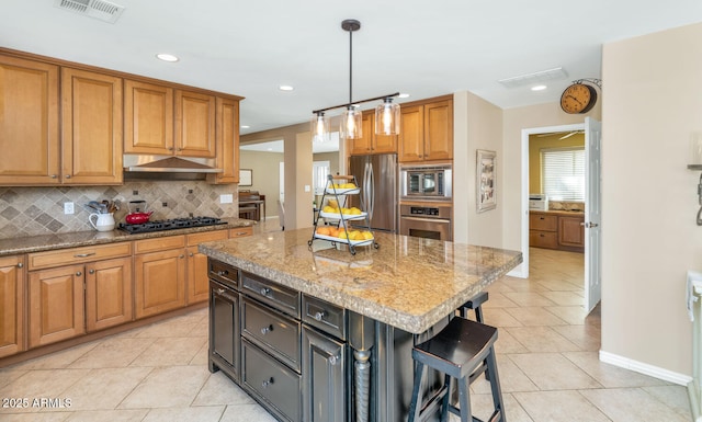 kitchen with hanging light fixtures, stainless steel appliances, a kitchen island, light stone counters, and decorative backsplash