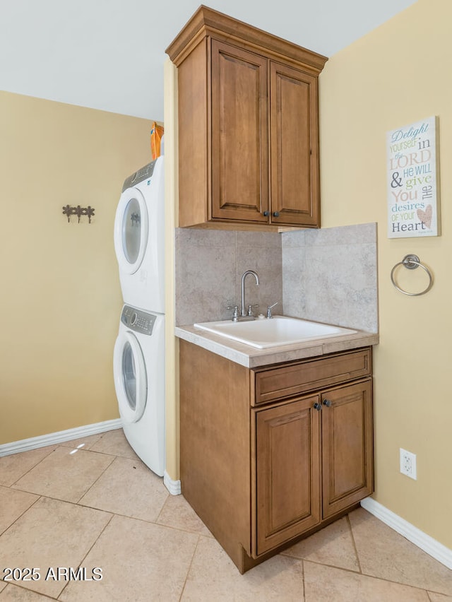 clothes washing area featuring light tile patterned flooring, cabinets, stacked washer and dryer, and sink