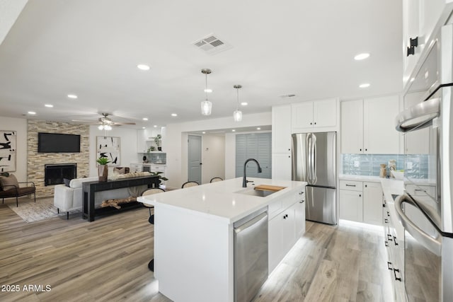 kitchen with appliances with stainless steel finishes, decorative light fixtures, white cabinetry, sink, and a kitchen island with sink