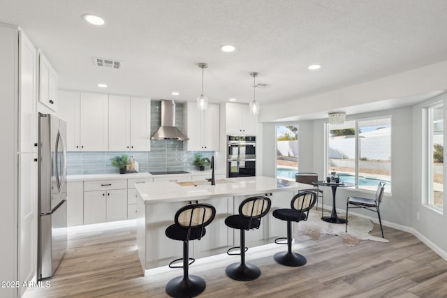 kitchen with wall chimney exhaust hood, a breakfast bar area, hanging light fixtures, stainless steel appliances, and a kitchen island with sink