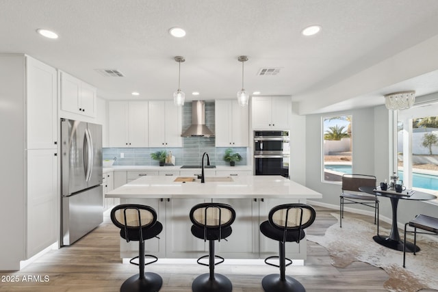 kitchen featuring white cabinetry, hanging light fixtures, stainless steel appliances, and wall chimney exhaust hood