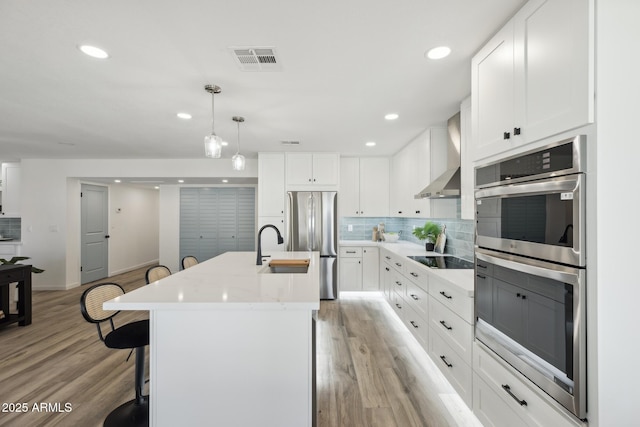 kitchen with white cabinetry, backsplash, hanging light fixtures, stainless steel appliances, and a center island with sink