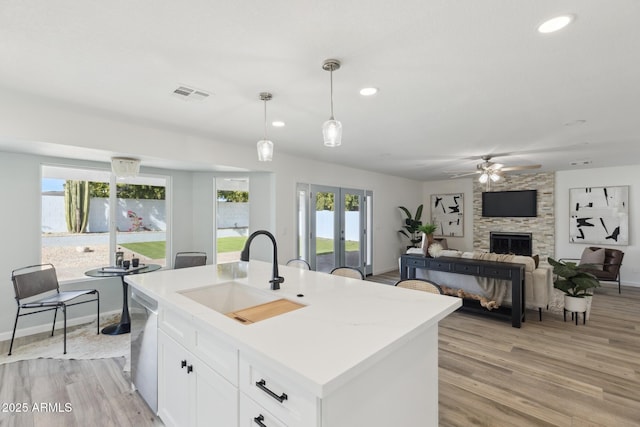 kitchen with an island with sink, dishwasher, sink, white cabinetry, and hanging light fixtures