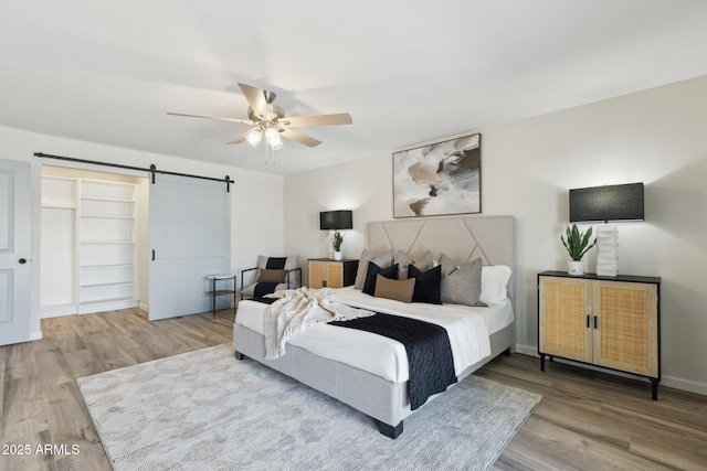 bedroom featuring hardwood / wood-style flooring, ceiling fan, and a barn door