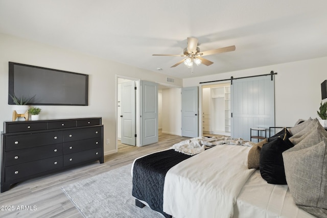 bedroom featuring ceiling fan, a barn door, and light wood-type flooring