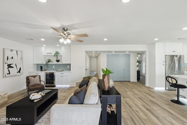 living room with wine cooler, ceiling fan, and light wood-type flooring