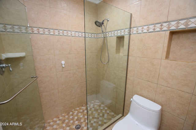 bathroom featuring tiled shower, toilet, and tile walls