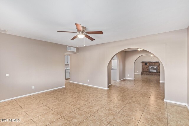 tiled spare room with ceiling fan and a brick fireplace