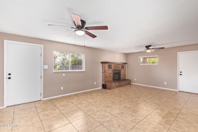 unfurnished living room featuring ceiling fan, light tile patterned flooring, plenty of natural light, and a brick fireplace