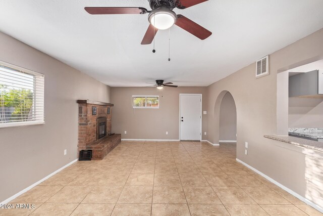 unfurnished living room featuring ceiling fan, a wealth of natural light, light tile patterned flooring, and a brick fireplace