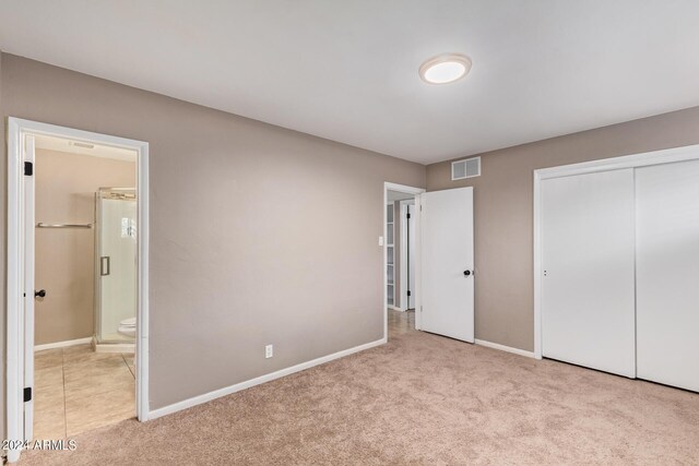 unfurnished bedroom featuring a closet, light carpet, and ensuite bathroom