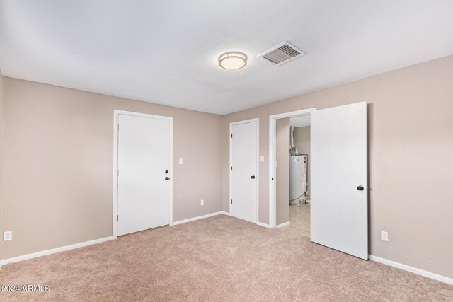 unfurnished bedroom featuring light colored carpet and water heater