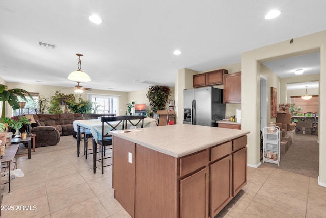 kitchen with visible vents, a kitchen island, light countertops, decorative light fixtures, and refrigerator with ice dispenser