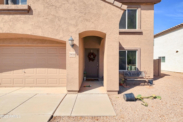 view of exterior entry featuring stucco siding, driveway, and a garage