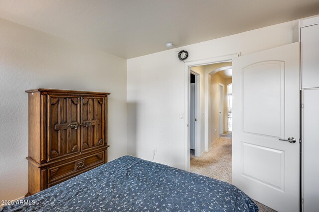 bedroom featuring arched walkways and light carpet