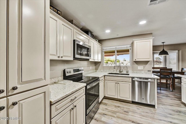 kitchen with visible vents, light wood-type flooring, a sink, light stone counters, and stainless steel appliances