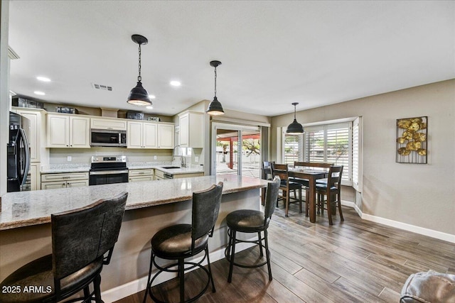 kitchen with a kitchen bar, visible vents, light stone countertops, baseboards, and stainless steel appliances
