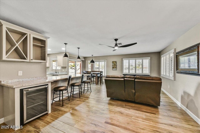 living area featuring wine cooler, baseboards, recessed lighting, a ceiling fan, and light wood finished floors