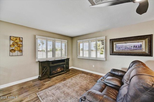 living room with a glass covered fireplace, baseboards, wood finished floors, and a wealth of natural light