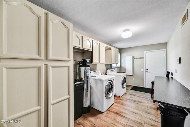 washroom with visible vents, washer and clothes dryer, light wood finished floors, and cabinet space