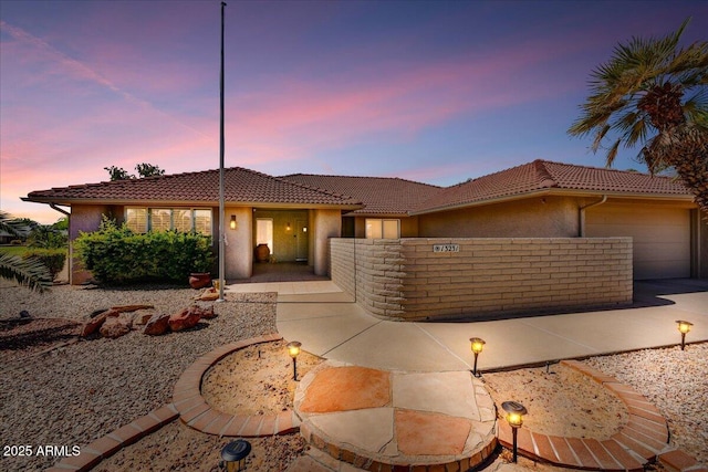 view of front facade with stucco siding, driveway, a tile roof, and a garage