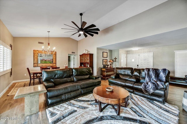 living area with visible vents, light wood-style floors, baseboards, ceiling fan with notable chandelier, and vaulted ceiling