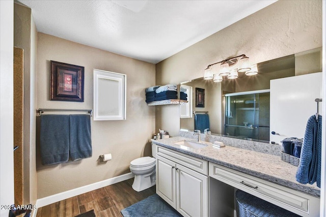 bathroom featuring a stall shower, wood finished floors, vanity, baseboards, and toilet