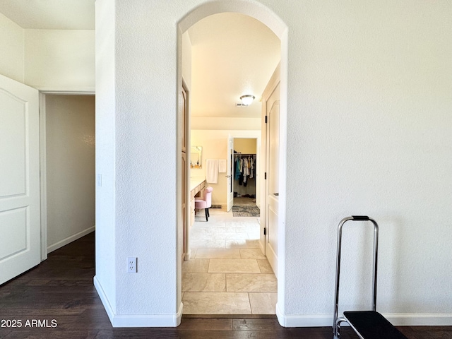 corridor featuring wood finished floors, arched walkways, and baseboards