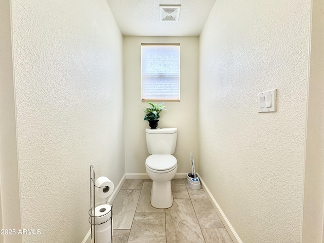 bathroom with toilet, baseboards, visible vents, and a textured wall