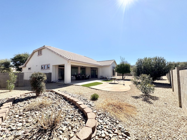 rear view of house featuring a tile roof, stucco siding, a fenced backyard, and a patio