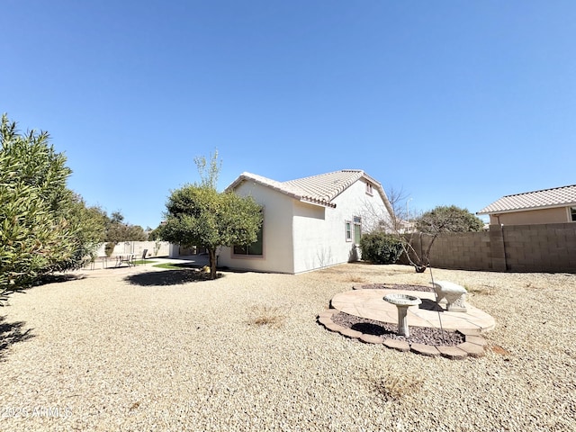 view of side of property featuring a patio area, stucco siding, a tiled roof, and fence