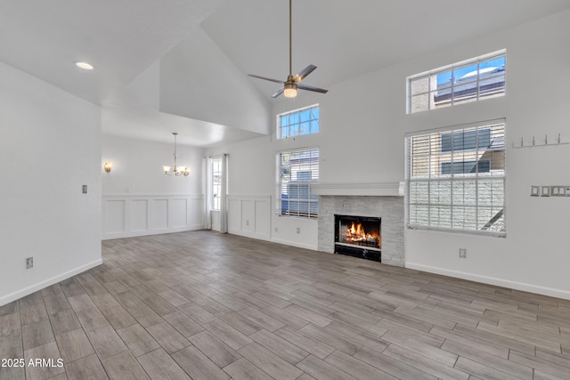 unfurnished living room with a warm lit fireplace, high vaulted ceiling, a decorative wall, ceiling fan with notable chandelier, and wood finished floors