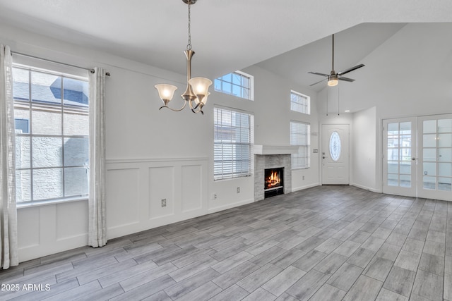 unfurnished living room featuring a tile fireplace, ceiling fan with notable chandelier, a decorative wall, and wood finish floors