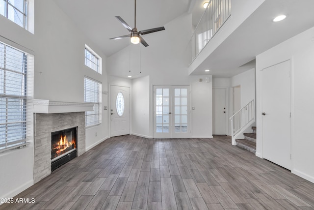 unfurnished living room featuring a wealth of natural light, stairs, wood finished floors, and a tile fireplace