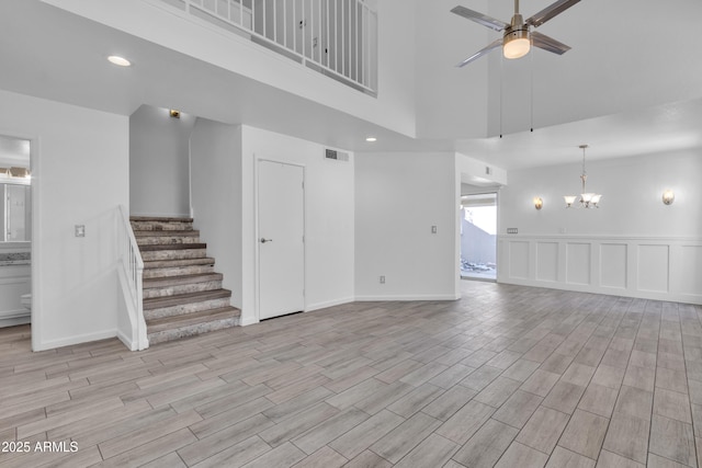 unfurnished living room with light wood finished floors, visible vents, stairway, a decorative wall, and ceiling fan with notable chandelier