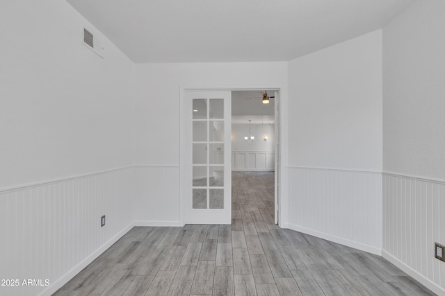 empty room with ceiling fan with notable chandelier, wainscoting, wood finished floors, and visible vents