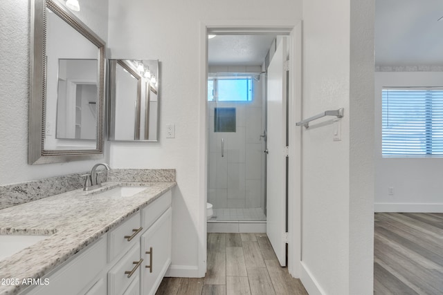 full bathroom with double vanity, toilet, a sink, a shower stall, and wood finished floors