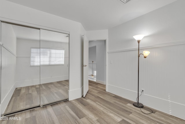 unfurnished bedroom featuring a wainscoted wall, a closet, and wood finished floors