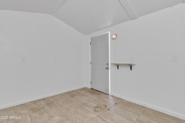 empty room with vaulted ceiling, baseboards, and light tile patterned floors