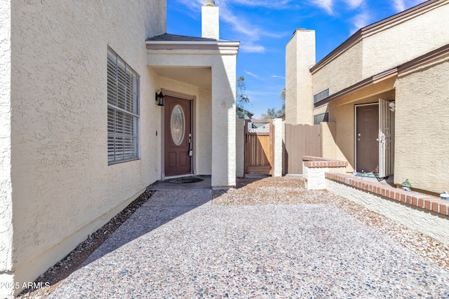 entrance to property featuring a gate, a chimney, and stucco siding