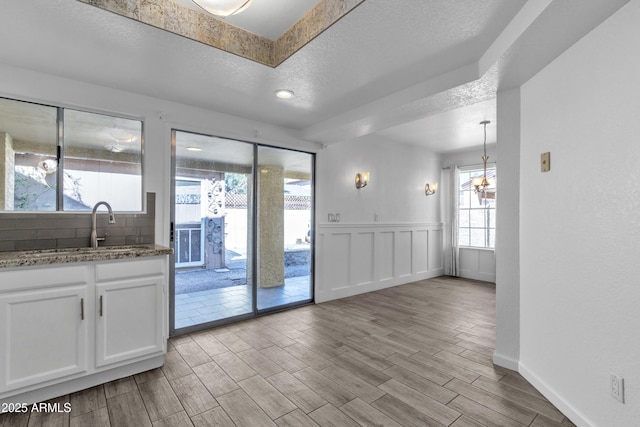 interior space with a textured ceiling, a decorative wall, a sink, wood tiled floor, and an inviting chandelier