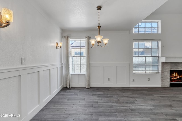 unfurnished dining area featuring a textured ceiling, a decorative wall, wood finish floors, a lit fireplace, and an inviting chandelier