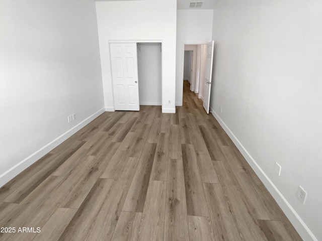 unfurnished bedroom with a closet, visible vents, baseboards, and wood finished floors